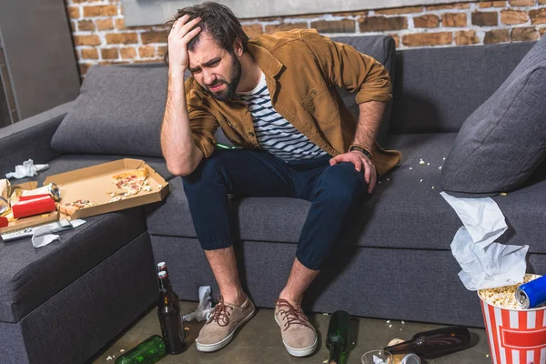 Schöner Einzelgänger, der morgens Kopfschmerzen hat und im Wohnzimmer auf dem Sofa sitzt — Stockfoto