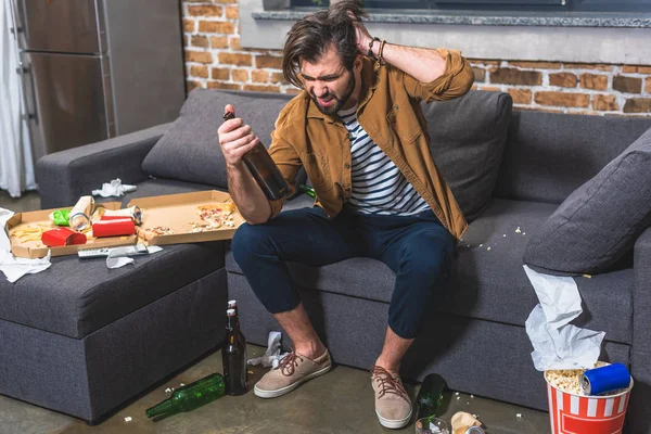 Solitário com ressaca olhando para garrafa de vinho na sala de estar — Fotografia de Stock