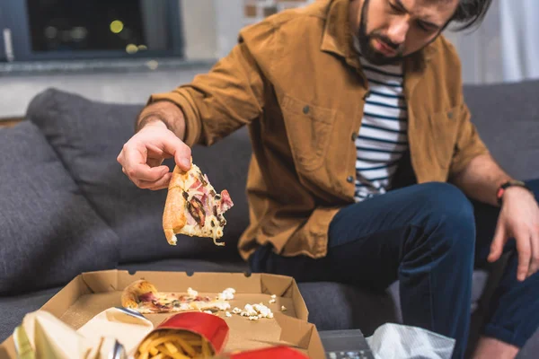 Imagem cortada de solitário irritado tomando pedaço de pizza na sala de estar — Fotografia de Stock