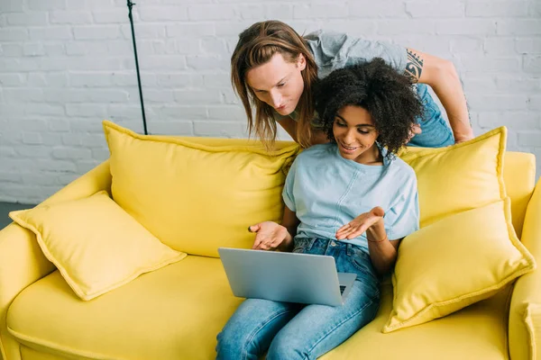 Attractive african american woman pointing on laptop screen to boyfriend — Stock Photo