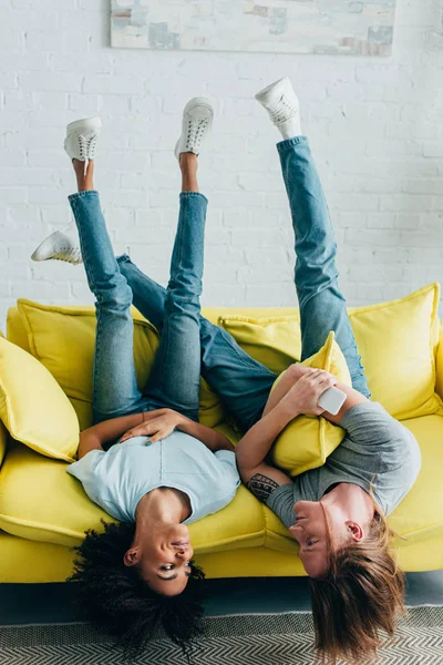 Junge Frau mit Freund hält Smartphone und legt sich kopfüber auf Sofa — Stockfoto