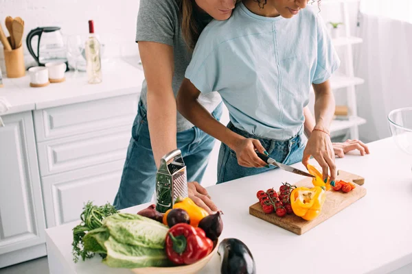 Cropped shot of young woman cutting bell pepper while boyfriend standing behind at kitchen — Stock Photo