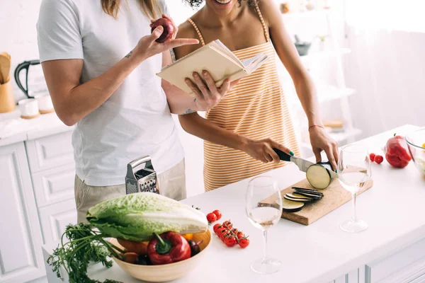 Recortado tiro de hombre con cebolla apuntando en receta en libro a novia corte berenjena - foto de stock