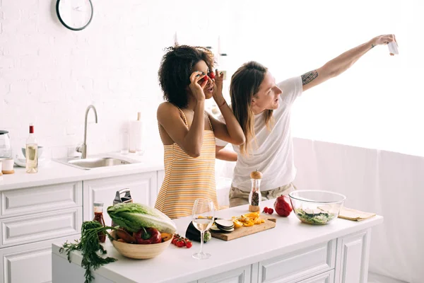 Young man taking selfie on smartphone with girlfriend covering eyes by cherry tomatoes — Stock Photo