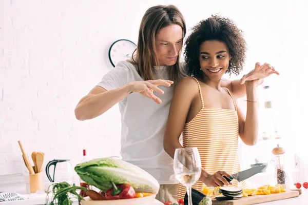 Smiling african american woman holding boyfriend while he gesturing by hands at kitchen — Stock Photo