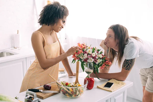 Young man gifting bouquet of flowers to african american girlfriend at kitchen — Stock Photo