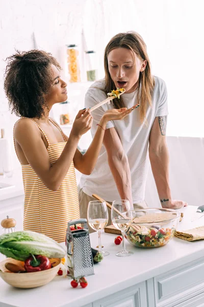 Happy african american woman feeding boyfriend with tattooed hand — Stock Photo