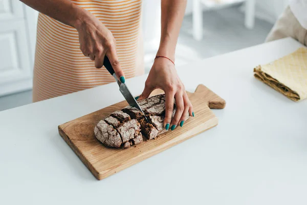 Tiro cortado de mulher cortando pão a bordo na cozinha — Fotografia de Stock