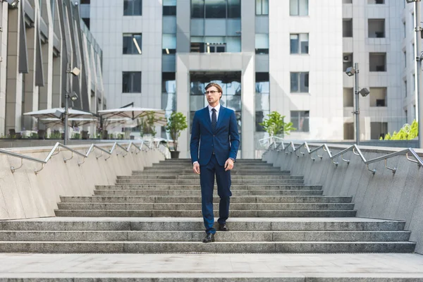 Apuesto joven hombre de negocios caminando por las escaleras en el distrito de negocios - foto de stock