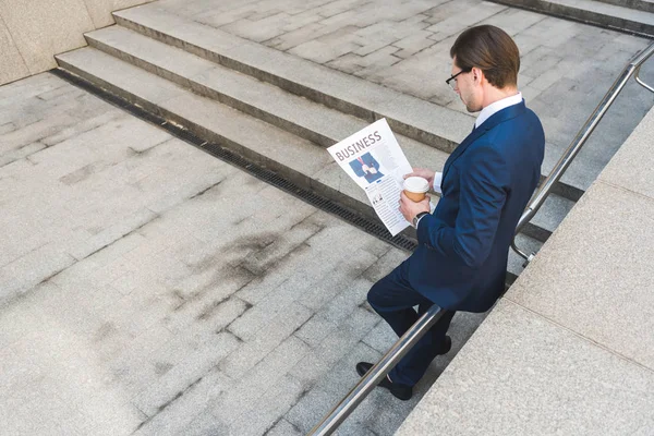 Високий кут зору молодого бізнесмена з кавою, щоб піти читати газету — стокове фото