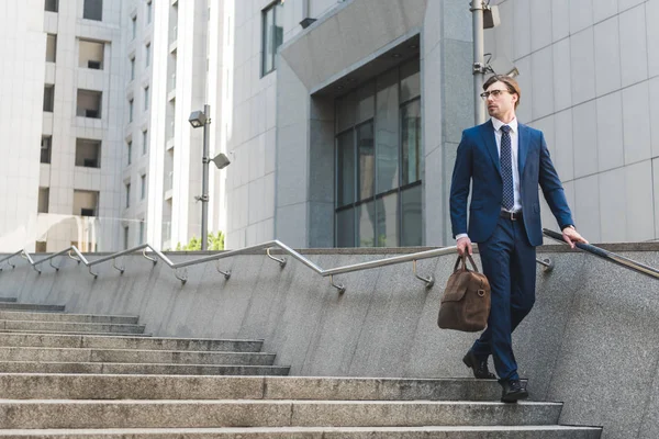 Attractive young businessman in stylish suit with briefcase in business district — Stock Photo
