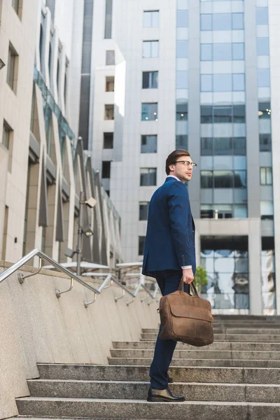 Bel homme d'affaires en costume élégant avec mallette en cuir montant les escaliers — Photo de stock