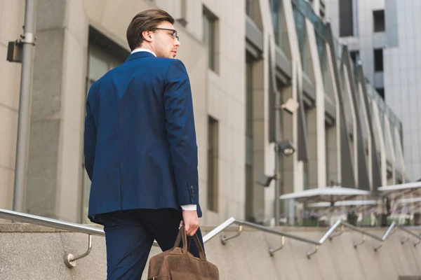 Hombre de negocios en traje elegante con maletín de cuero subiendo escaleras - foto de stock