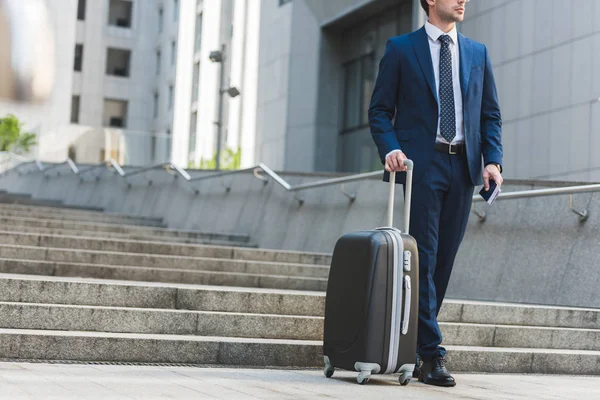 Tiro recortado de hombre de negocios con equipaje y billetes de avión a pie por distrito de negocios — Stock Photo