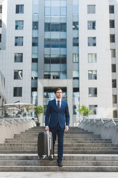 Stylish young businessman with luggage walking by business district — Stock Photo