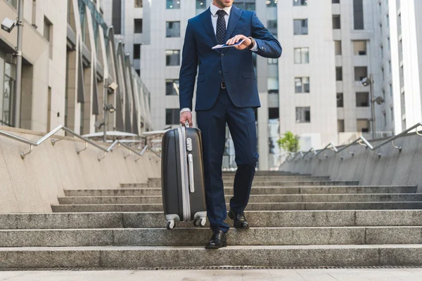 Обрезанный снимок бизнесмена в стильном костюме с багажом и авиабилетами спускающимся по лестнице в деловой район — стоковое фото