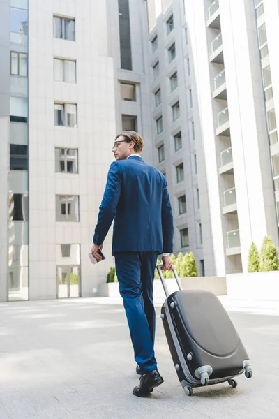 Joven hombre de negocios guapo con equipaje caminando por el distrito de negocios - foto de stock