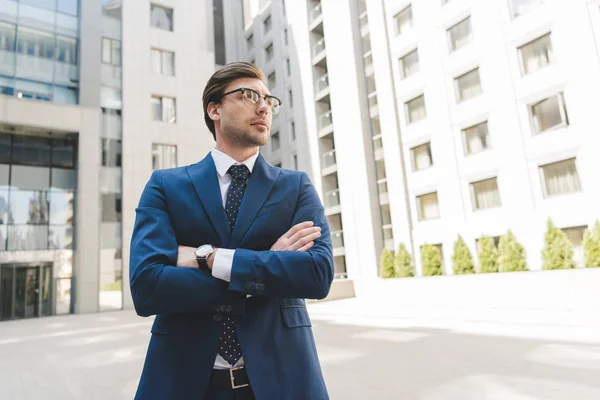 Bottom view of serious young businessman in stylish suit with crossed arms — Stock Photo