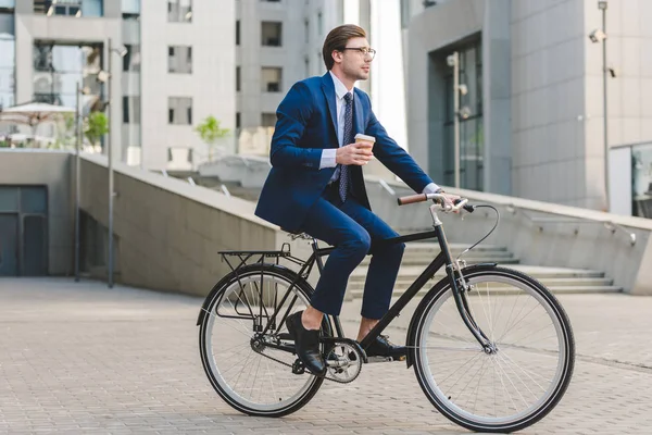 Young businessman in stylish suit with coffee to go sitting on vintage bicycle — Stock Photo