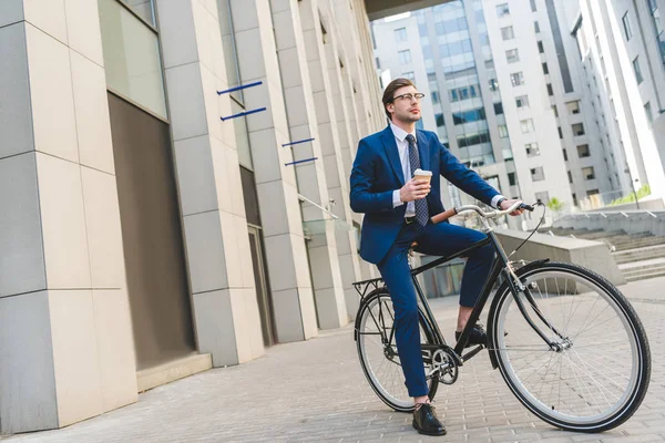 Handsome young businessman in stylish suit with coffee to go sitting on vintage bicycle — Stock Photo