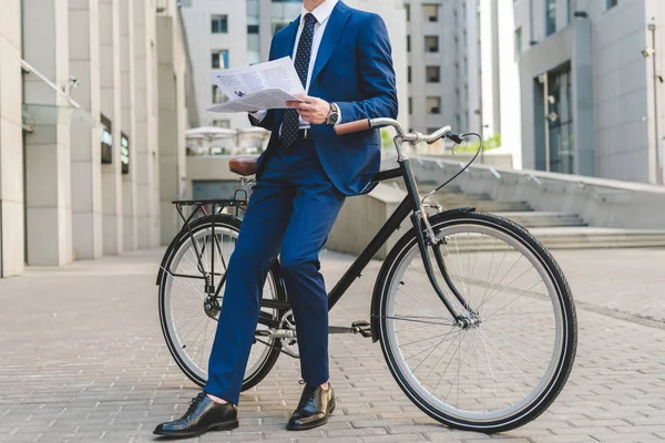 Schnappschuss von Geschäftsmann im schicken Anzug mit Zeitung an Fahrrad gelehnt — Stockfoto