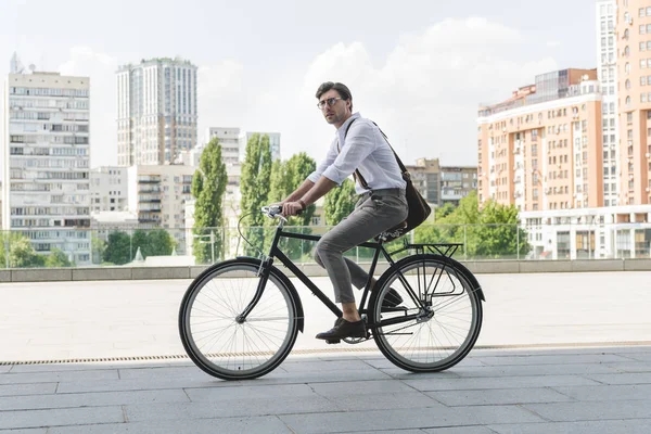 Вид збоку привабливого молодого чоловіка в стильному одязі, що їде вінтажний велосипед на міській вулиці — стокове фото