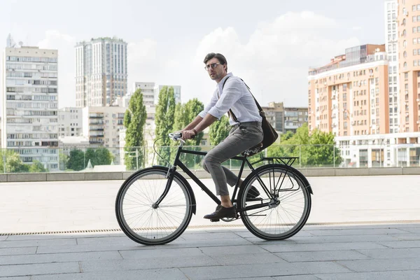 Side view of attractive young man in stylish clothes riding vintage bicycle on city street — Stock Photo