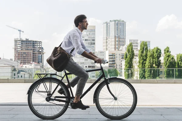 Вид сбоку на молодого человека в стильной одежде на велосипеде на городской улице — стоковое фото