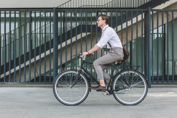 Вид сбоку красивого молодого человека, катающегося на винтажном велосипеде по городской улице — стоковое фото