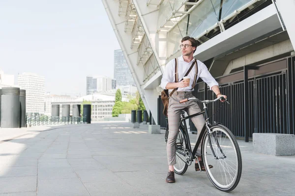 Schöner junger Mann mit Pappbecher Kaffee auf Oldtimer-Fahrrad in der Nähe des Sportstadions Gebäude — Stockfoto