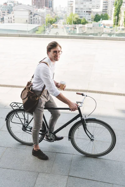 Высокий угол обзора привлекательного молодого человека с бумажной чашкой кофе на винтажном велосипеде — стоковое фото