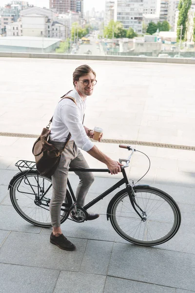 Vista de ángulo alto de joven atractivo con taza de papel de café en bicicleta vintage - foto de stock