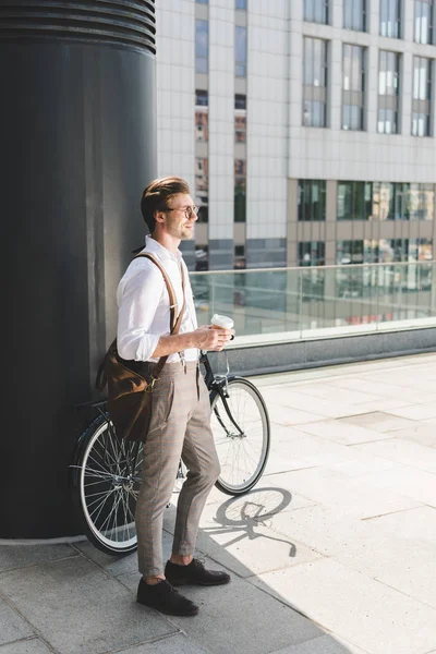 Stylish young man with coffee to go and vintage bicycle on rooftop of business building — Stock Photo