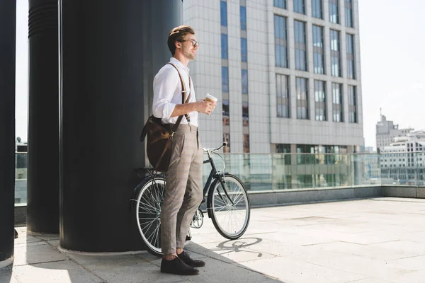 Smiling young man with coffee to go and vintage bicycle on rooftop of business building — Stock Photo
