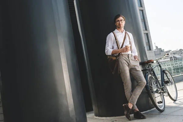 Handsome young man with coffee to go and vintage bicycle on rooftop of business building — Stock Photo