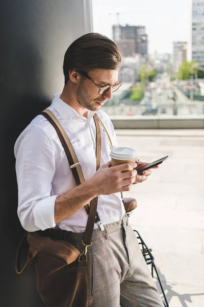 Joven con estilo con taza de papel de café para ir con el teléfono inteligente - foto de stock