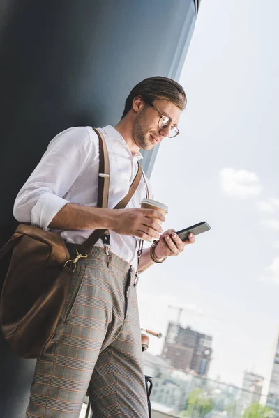 Vue du bas de beau jeune homme avec du café pour aller à l'aide d'un smartphone — Photo de stock