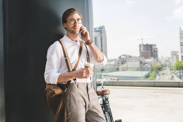 Joven feliz con café para ir a hablar por teléfono en la azotea del edificio de negocios - foto de stock