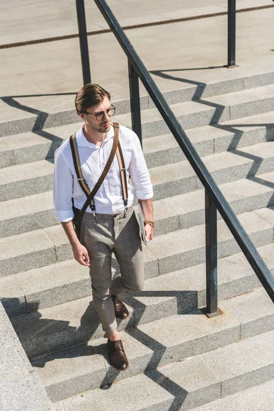 Vue grand angle de beau jeune homme avec ordinateur portable plié marchant sur les escaliers dans la rue de la ville — Photo de stock