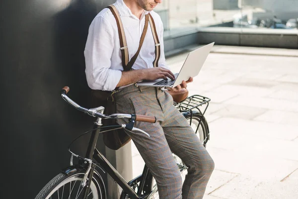 Plan recadré de l'homme travaillant avec un ordinateur portable tout en s'appuyant sur un vélo vintage — Photo de stock