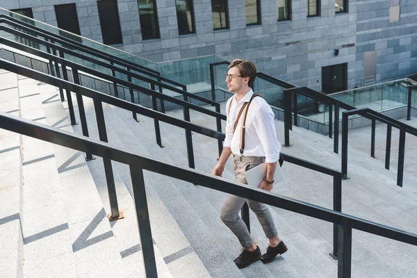 Handsome young man walking on stairs with laptop on city street — Stock Photo