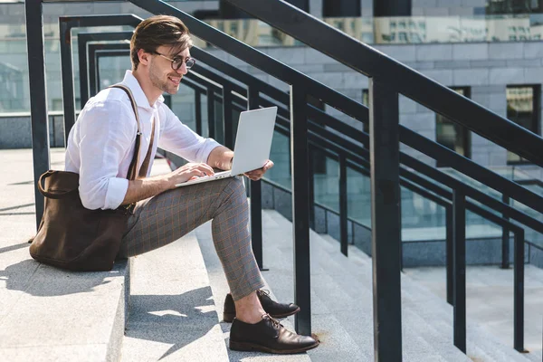 Beau jeune homme travaillant avec ordinateur portable sur les escaliers dans la rue de la ville — Photo de stock