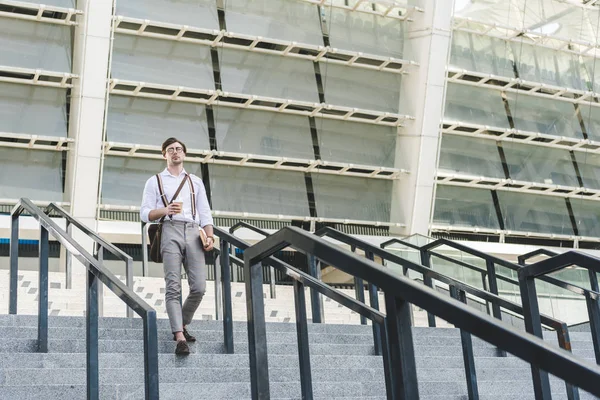Joven guapo bajando escaleras frente al estadio con libro y café para llevar - foto de stock