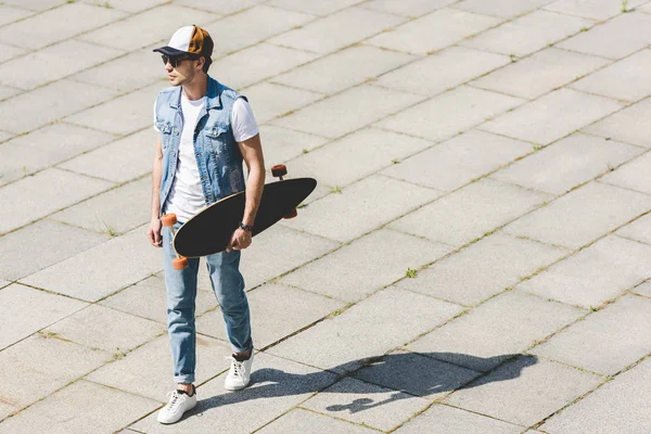 Высокий угол обзора красивого молодого человека, идущего со скейтбордом в руке — стоковое фото