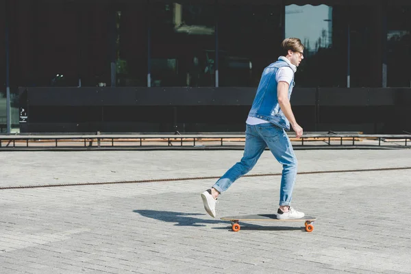Vista lateral do jovem skatista montando longboard por rua — Fotografia de Stock