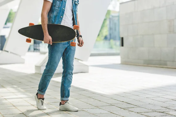 Обрезанный кадр фигуриста в джинсовой одежде со скейтбордом — стоковое фото