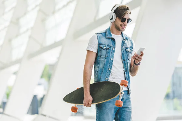 Jovem bonito com longboard usando smartphone na rua da cidade moderna — Fotografia de Stock