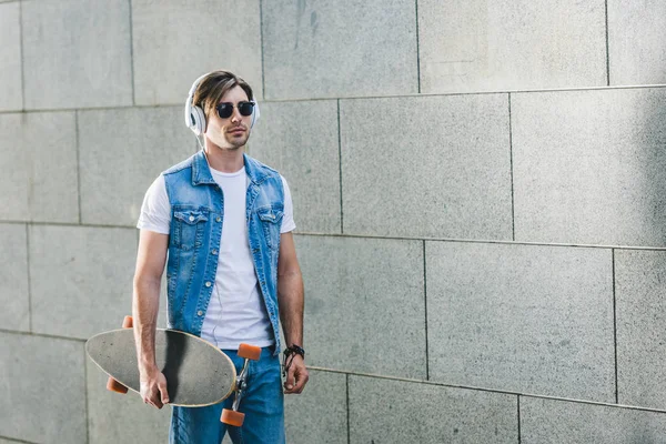 Handsome young skater in headphones with longboard — Stock Photo