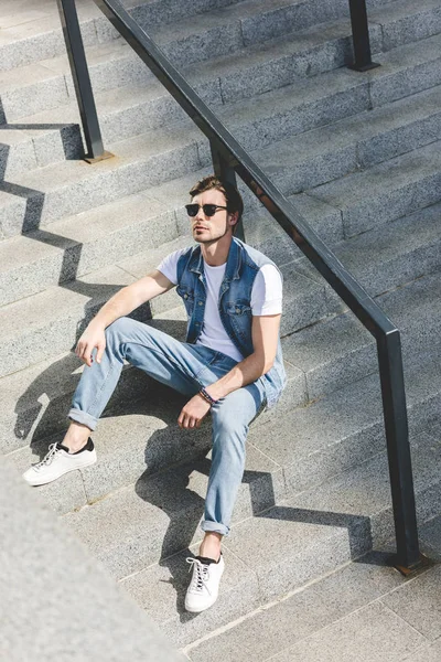 Schöner junger Mann sitzt auf einer Treppe und schaut nach oben — Stockfoto