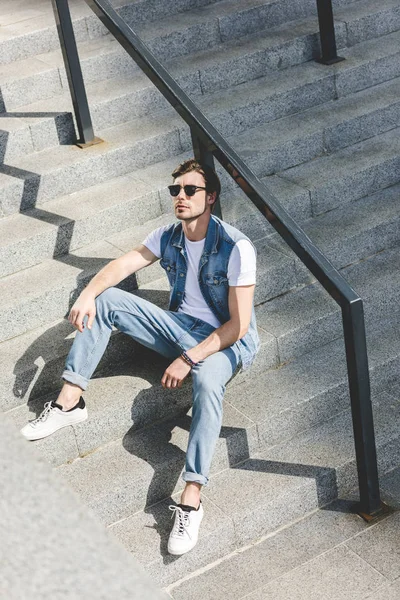 Joven guapo sentado en las escaleras y mirando hacia arriba - foto de stock